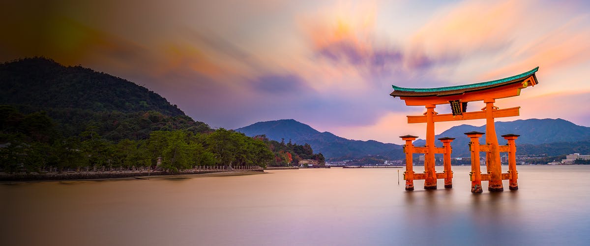 Torii gate at sunset on Miyajima Island, Hiroshima, with mountains in the background.